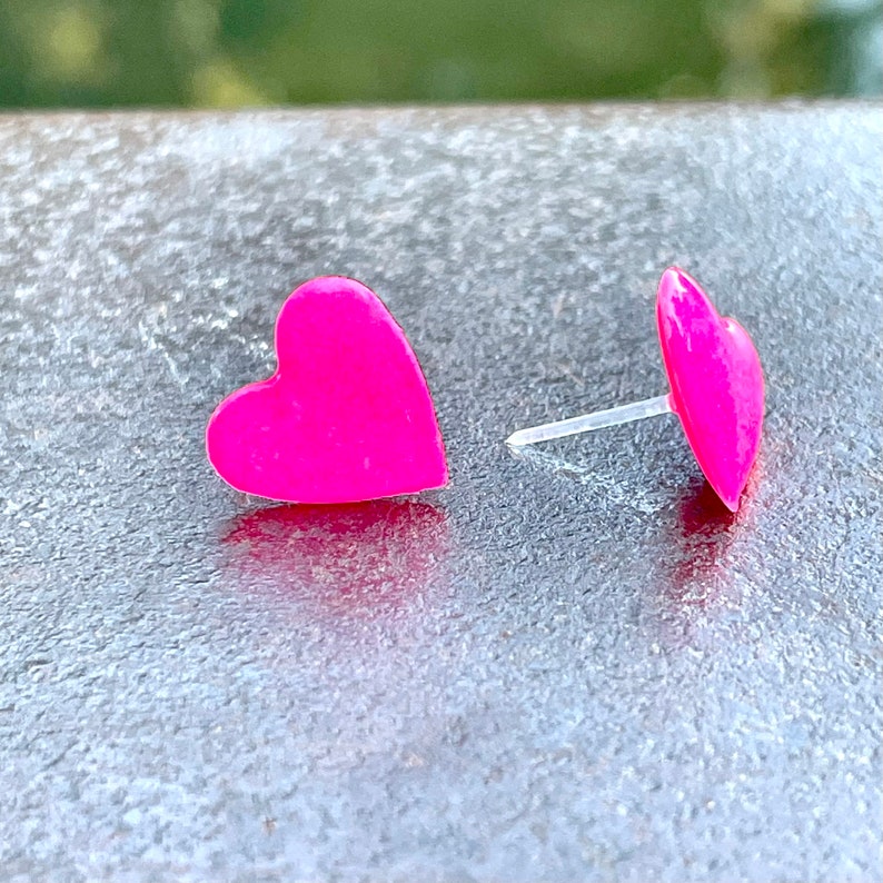 May include: A pair of pink heart-shaped stud earrings. The earrings are made of a shiny, smooth material.