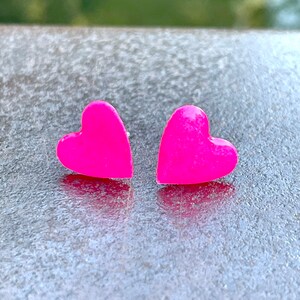 May include: A pair of pink heart-shaped earrings. The earrings are made of a shiny, smooth material.