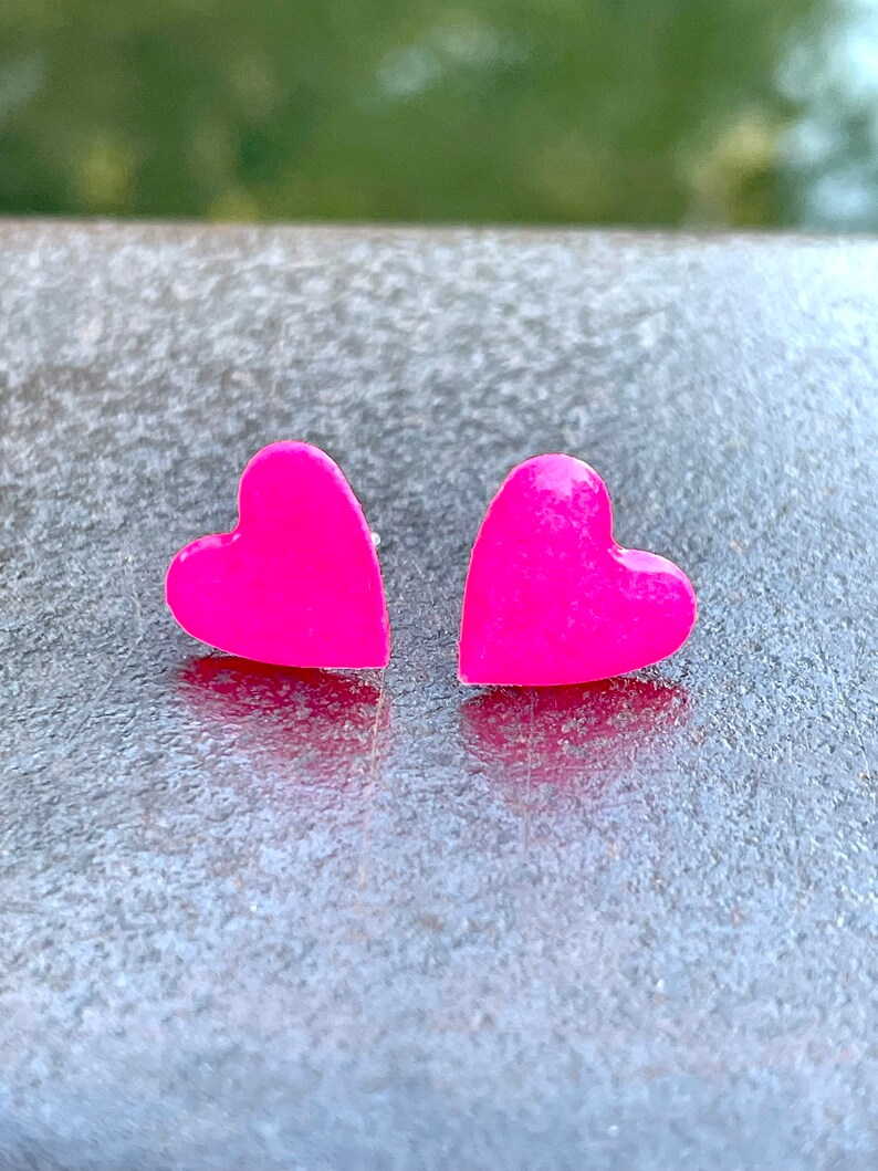 May include: A pair of pink heart-shaped earrings. The earrings are made of a shiny, smooth material.