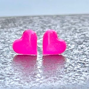 Puede incluir: Un par de pendientes de bot&oacute;n en forma de coraz&oacute;n rosa.