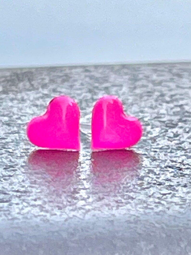 Puede incluir: Un par de pendientes de bot&oacute;n en forma de coraz&oacute;n rosa.