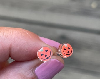 Op de afbeelding: Een paar oranje pompoenvormige oorbel studs met een glimlachend jack-o'-lantern gezicht.