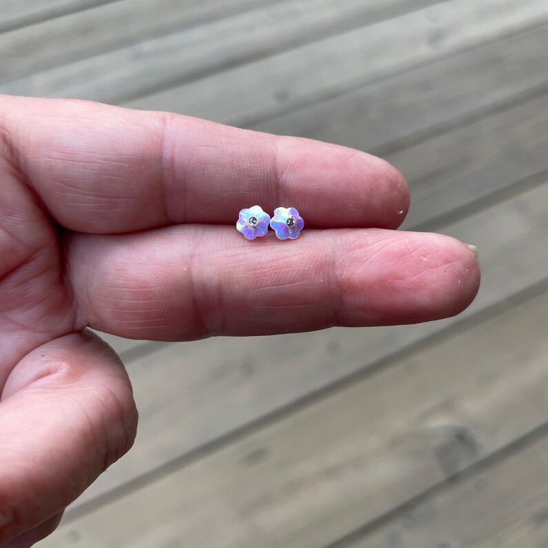 Pu&ograve; includere: Un paio di orecchini a perno a forma di fiore iridescente con un piccolo strass trasparente al centro di ogni fiore.