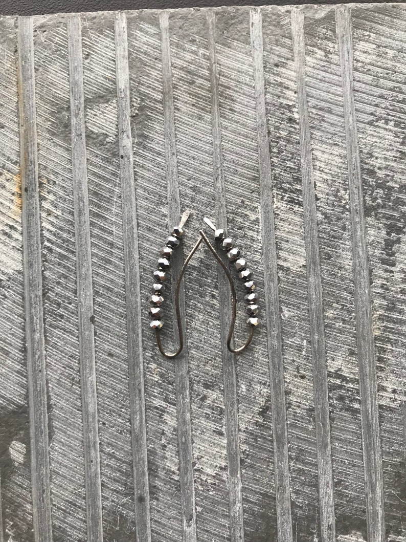 May include: A pair of silver earrings with a row of black beads hanging from each earring.