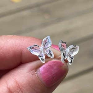 Op de afbeelding: Een paar zilveren vlinder oorringen met iriserende glitter accenten.