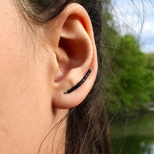 May include: A black ear cuff with small black beads. The cuff is curved and sits on the upper part of the ear.