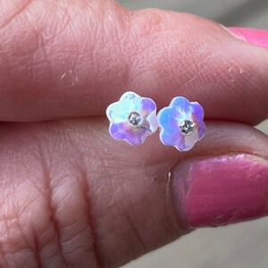 Pu&ograve; includere: Un paio di orecchini a forma di fiore iridescente con un cristallo di strass trasparente al centro di ogni fiore.