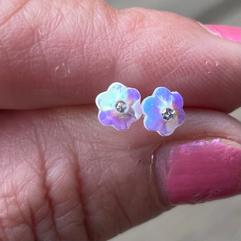 Pu&ograve; includere: Un paio di orecchini a forma di fiore iridescente con un cristallo di strass trasparente al centro di ogni fiore.