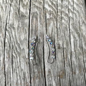May include: A pair of silver ear cuffs with clear crystal accents. The cuffs are curved and have a delicate design.
