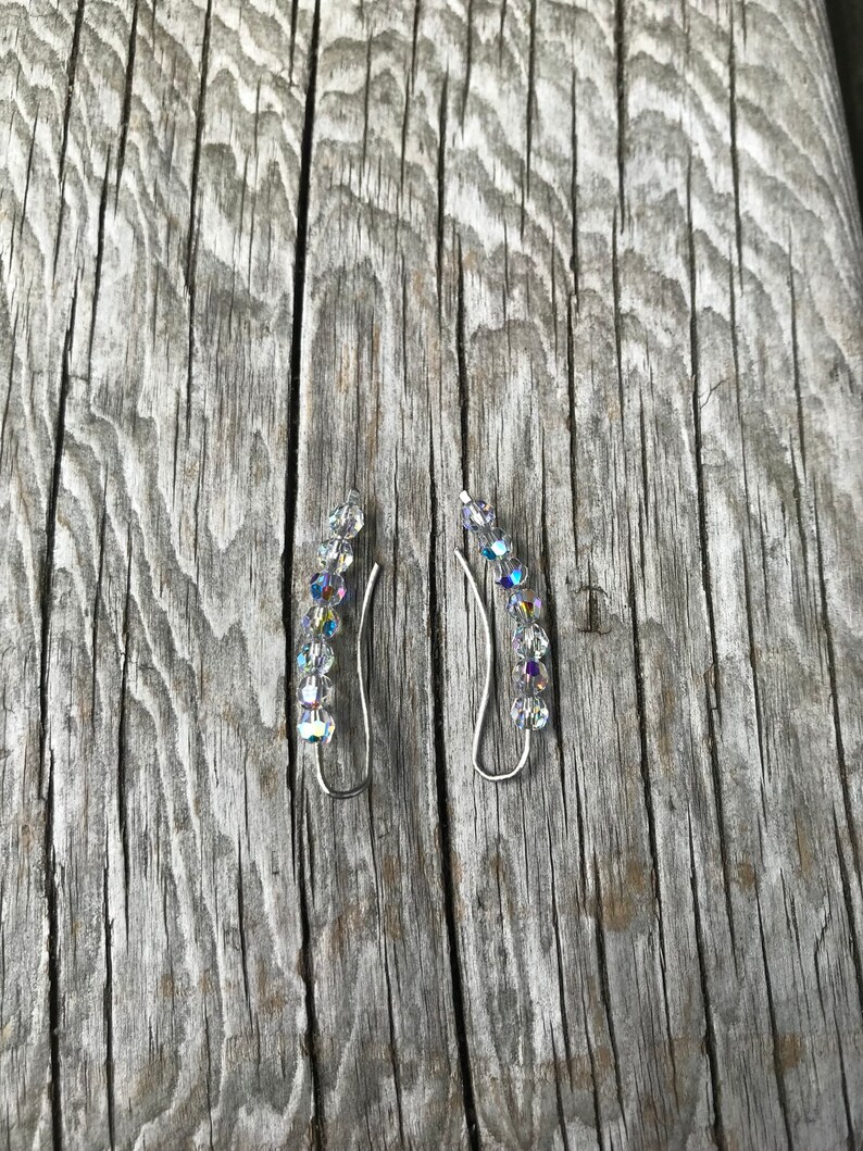 May include: A pair of silver ear cuffs with clear crystal accents. The cuffs are curved and have a delicate design.