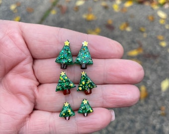 Op de afbeelding: Een set van vier groene glitter kerstboom oorbellen met gouden ster accenten. De oorbellen zijn in verschillende maten en worden getoond op een hand.
