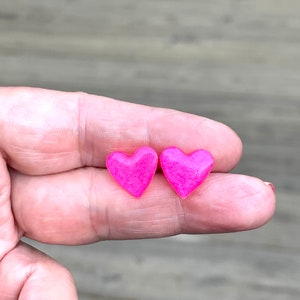 May include: A pair of pink heart-shaped earrings. The earrings are small and have a glossy finish.
