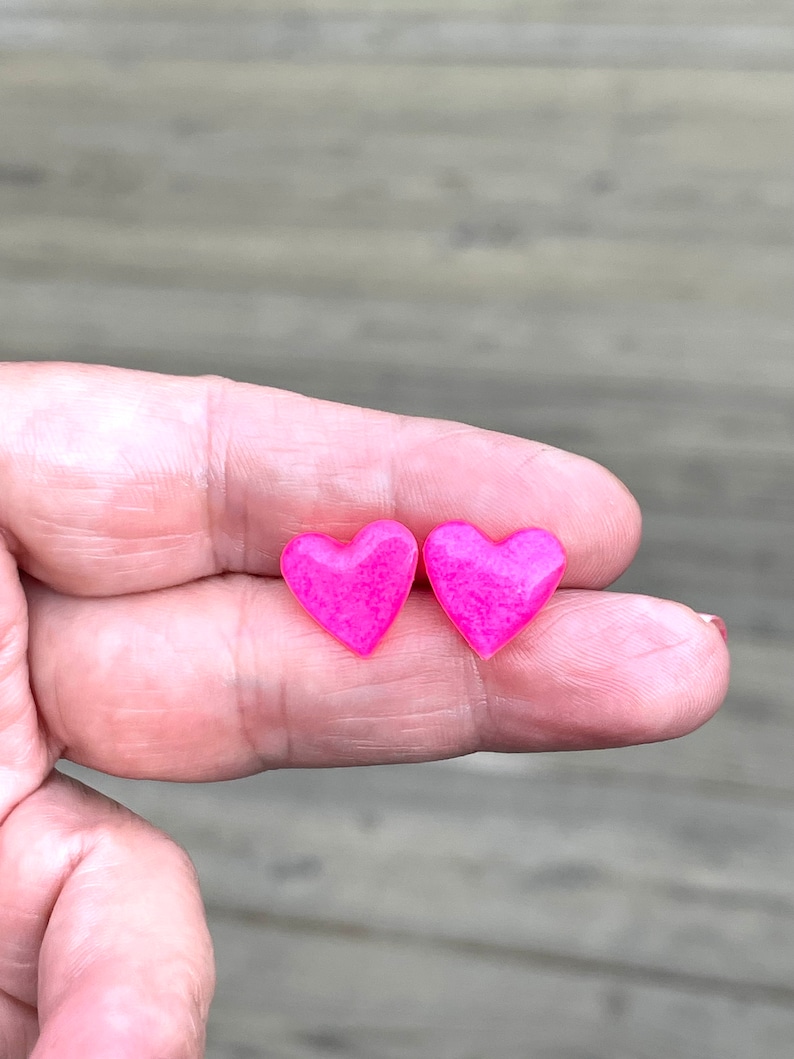 May include: A pair of pink heart-shaped earrings. The earrings are small and have a glossy finish.