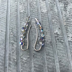 May include: A pair of silver earrings with a row of iridescent crystal beads hanging from each.