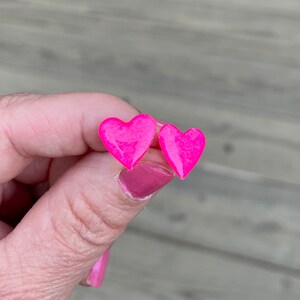 May include: A pair of pink heart-shaped stud earrings. The earrings are small and have a glossy finish.