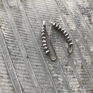 May include: A pair of silver earrings with a curved shape and a row of small, dark gray beads.