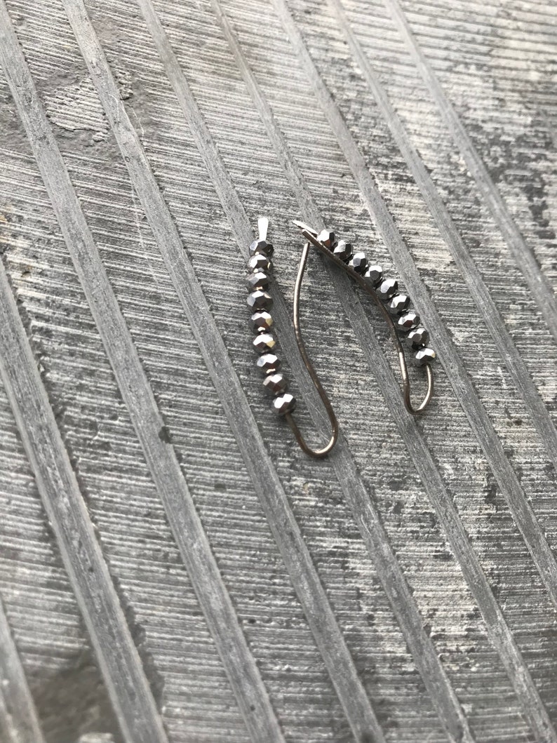 May include: A pair of silver earrings with a curved shape and a row of small, dark gray beads.