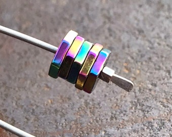Op de afbeelding: Een stapel van vijf regenboogkleurige zeshoekige metalen kralen op een zilveren draad.