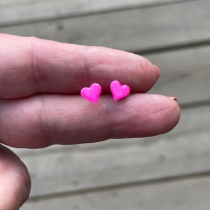 Puede incluir: Un par de pendientes de bot&oacute;n en forma de coraz&oacute;n rosa.