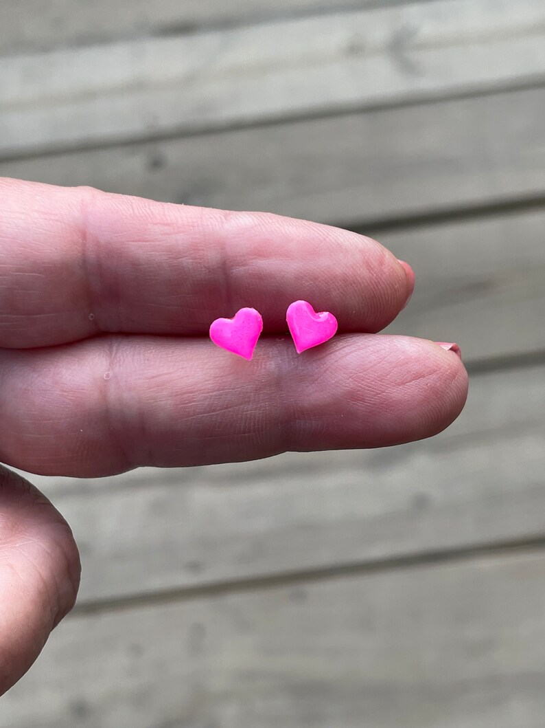 Puede incluir: Un par de pendientes de bot&oacute;n en forma de coraz&oacute;n rosa.