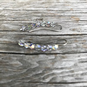 May include: A pair of silver ear cuffs with clear crystal beads. The cuffs are curved and have a delicate design.