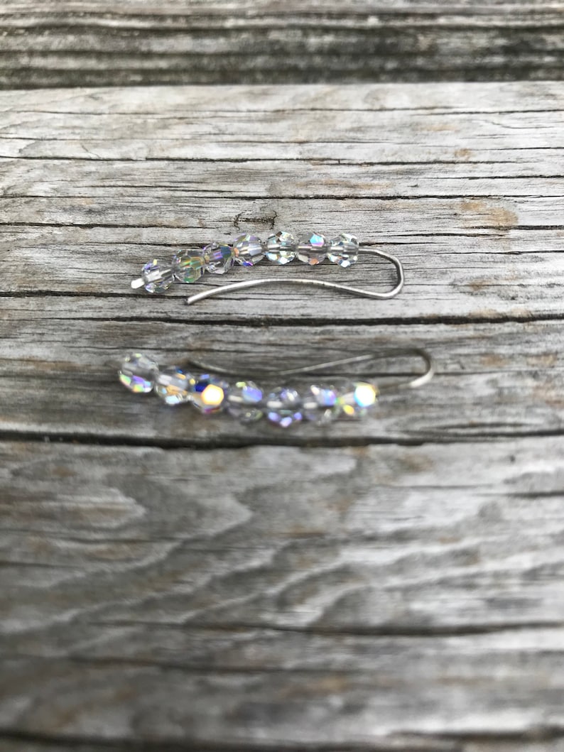 May include: A pair of silver ear cuffs with clear crystal beads. The cuffs are curved and have a delicate design.