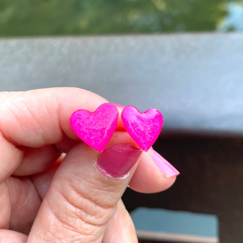 May include: A pair of pink heart-shaped stud earrings. The earrings are made of a sparkly, translucent material.