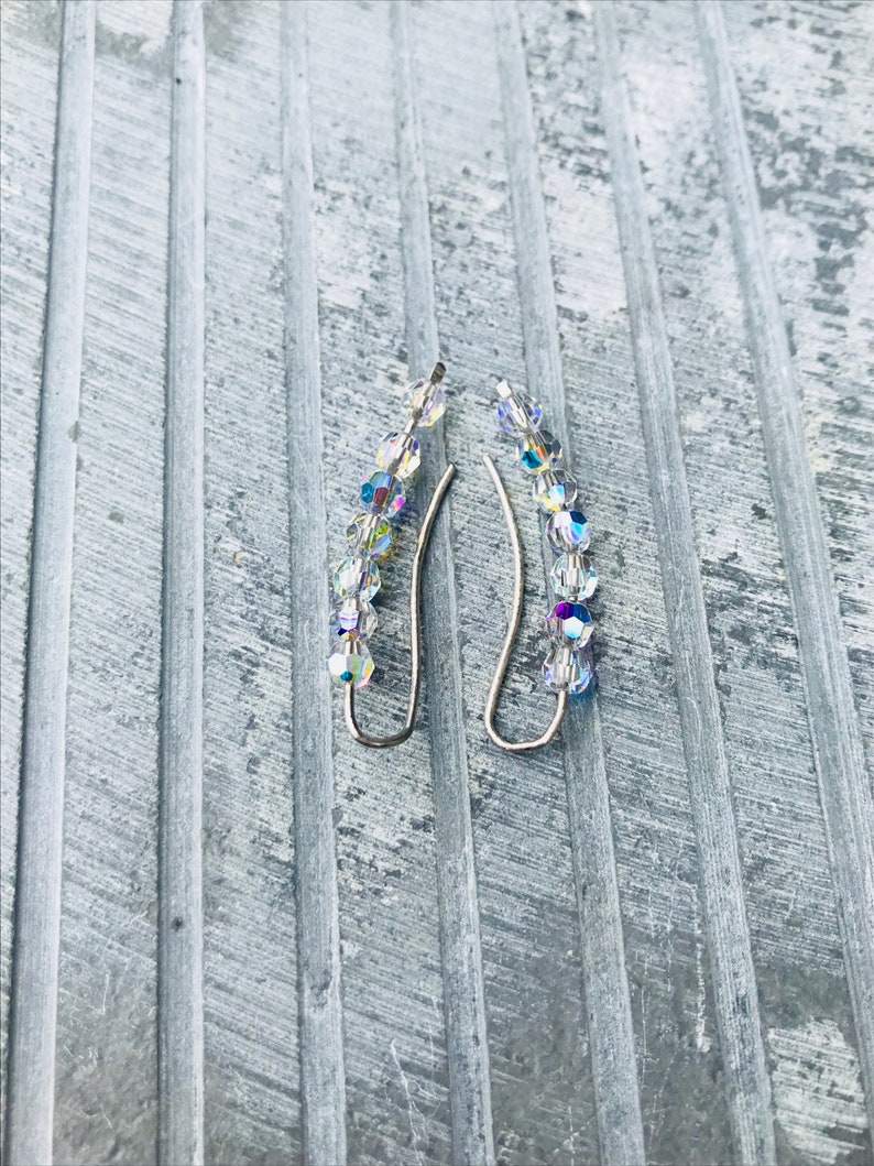 May include: A pair of silver earrings with iridescent crystal beads. The beads are arranged in a graduated pattern, with the largest bead at the bottom and the smallest bead at the top.