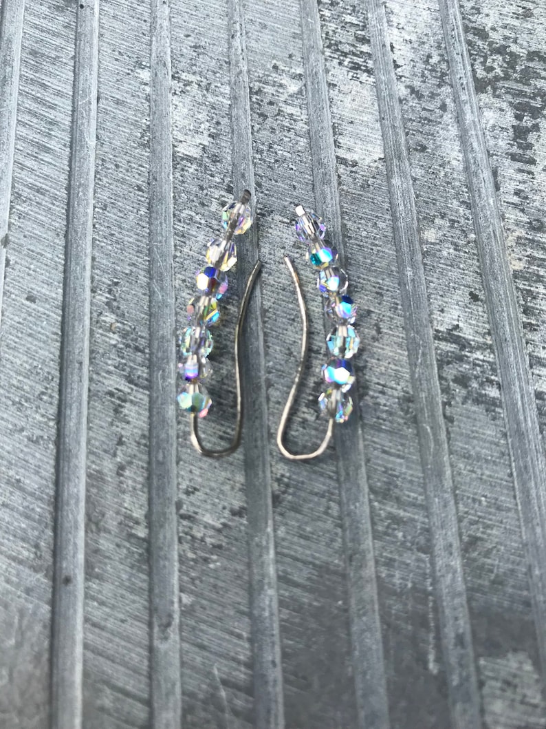 May include: A pair of silver earrings with a curved design. Each earring is adorned with a row of clear iridescent crystals.