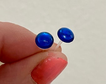 Op de afbeelding: Een paar kleine, ronde, blauwe glazen oorbellen met zilveren pinnen.