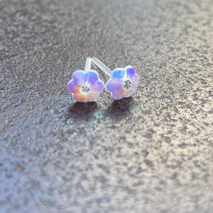 Pu&ograve; includere: Un paio di orecchini a perno a forma di fiore iridescente con strass trasparenti al centro.