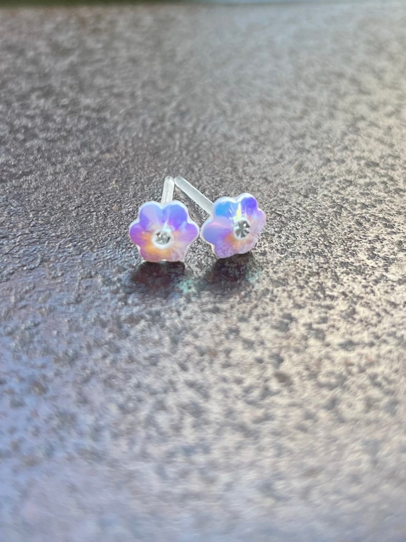 Pu&ograve; includere: Un paio di orecchini a perno a forma di fiore iridescente con strass trasparenti al centro.