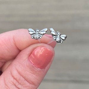 May include: A pair of silver bee stud earrings. The bees are facing forward with their wings spread out.