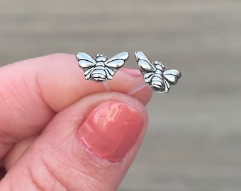 Op de afbeelding: Een paar zilveren bijen oorbel studs. De bijen kijken naar voren met hun vleugels uitgespreid.