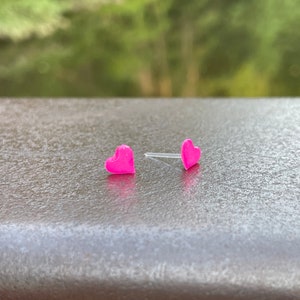 Puede incluir: Un par de pendientes de bot&oacute;n en forma de coraz&oacute;n rosa.