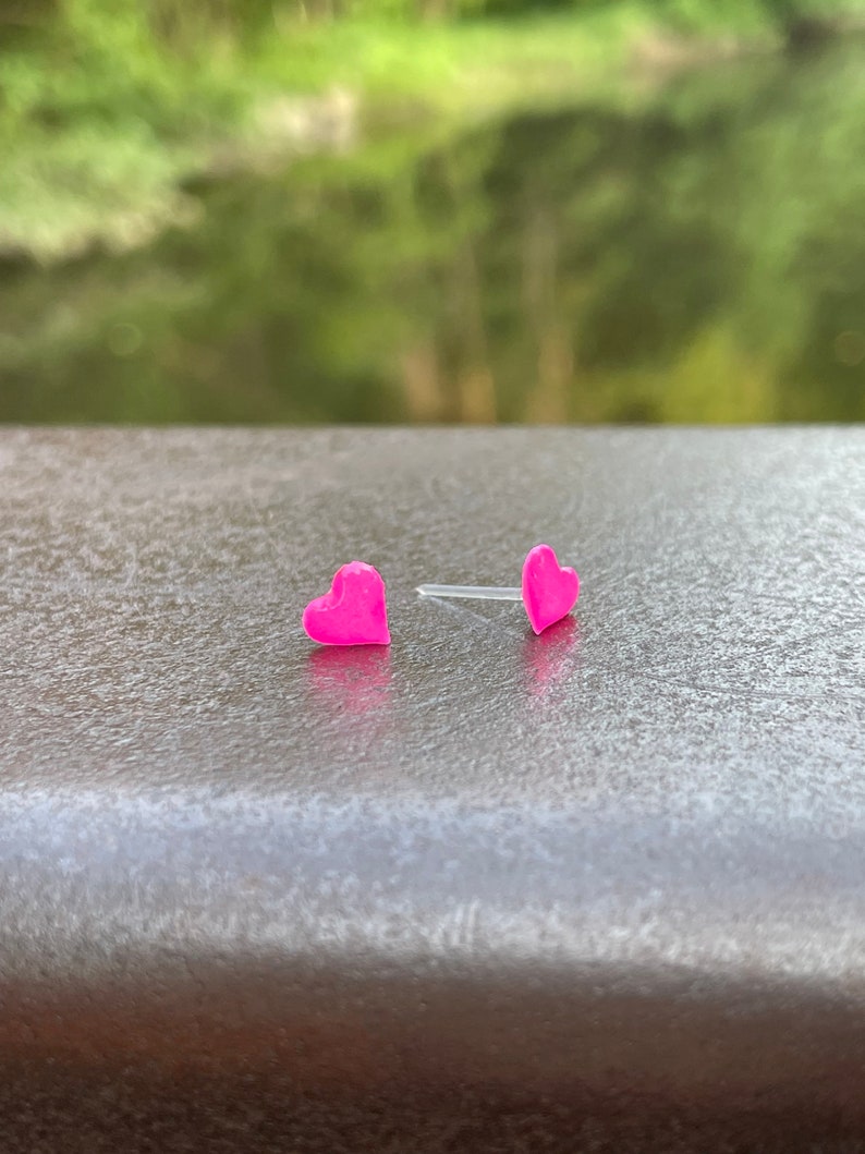 Puede incluir: Un par de pendientes de bot&oacute;n en forma de coraz&oacute;n rosa.