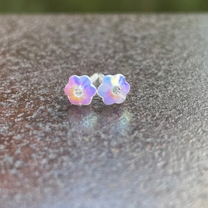 Pu&ograve; includere: Un paio di orecchini a perno a forma di fiore iridescente con un cristallo trasparente al centro di ogni fiore.