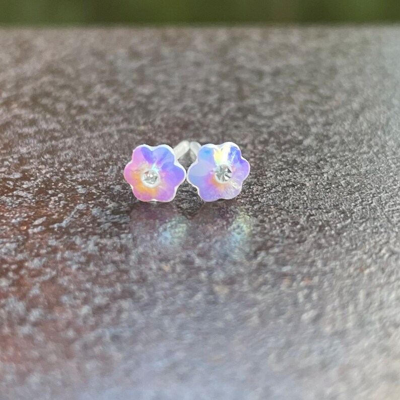 Pu&ograve; includere: Un paio di orecchini a perno a forma di fiore iridescente con un cristallo trasparente al centro di ogni fiore.