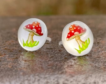 May include: A pair of stud earrings with a white background and a red and white mushroom illustration.