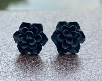 Op de afbeelding: Een paar zwarte oorbel studs in de vorm van een bloem. De oorbel studs zijn gemaakt van glad, mat materiaal.