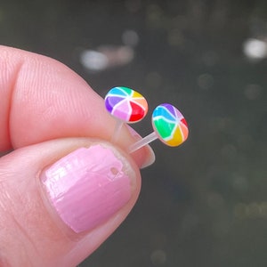 May include: A pair of rainbow-colored stud earrings. The earrings are small and round, with a white background and a rainbow design.