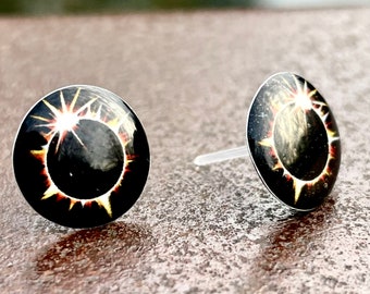 Op de afbeelding: Een paar zwarte oorbel studs met een gouden en oranje zonnestralen ontwerp.