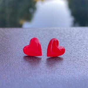May include: Two red heart-shaped earrings on a dark gray surface.