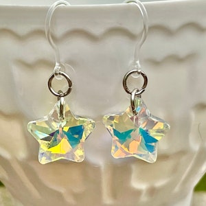 May include: A pair of silver star-shaped earrings with iridescent crystal accents. The earrings are on a white surface.