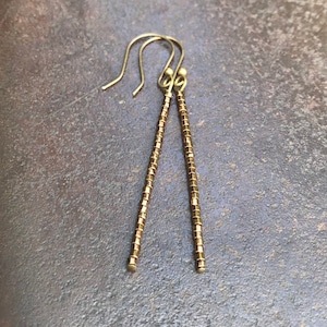 May include: A pair of gold-toned dangle earrings with a long, thin design. The earrings are made of small, round beads that are strung together.