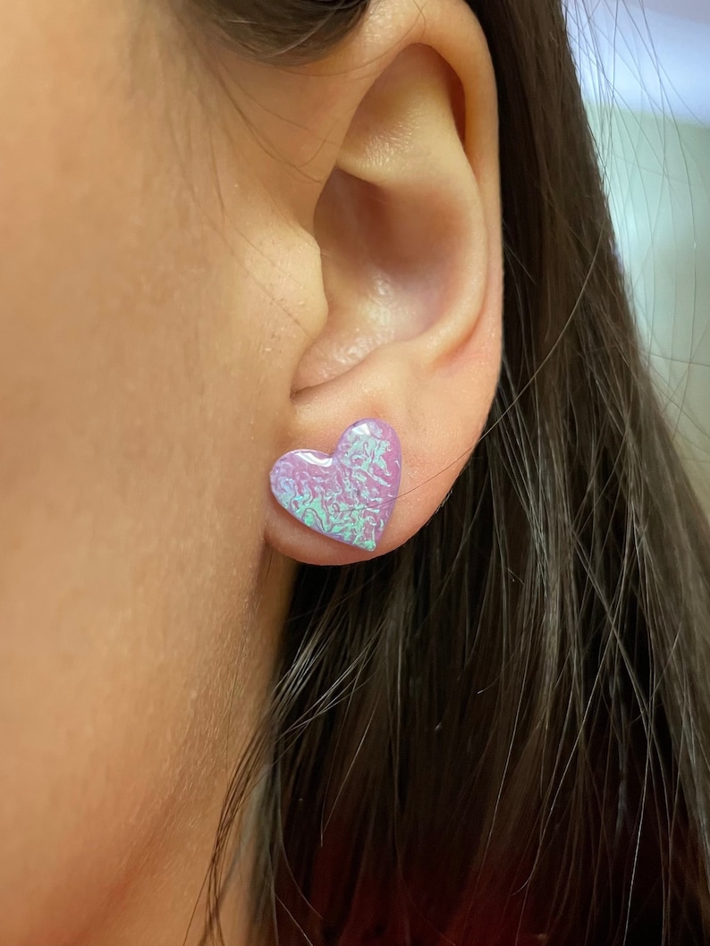 May include: A pair of iridescent purple heart-shaped earrings. The earrings are small and have a subtle shimmer.