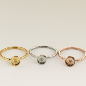 May include: Three rings with a round bezel setting. The rings are gold, silver, and rose gold.