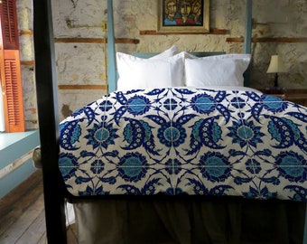 May include: A four-poster bed with a white and blue patterned duvet cover. The duvet cover features a traditional Turkish design with blue floral motifs on a white background. The bed is in a room with a rustic wooden wall and a framed painting above the headboard.