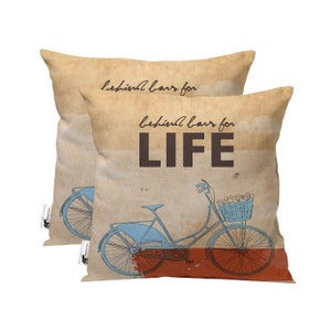 May include: Two beige throw pillows with a vintage design. The pillows feature a blue bicycle with a basket of flowers and the text "behind bars for LIFE".