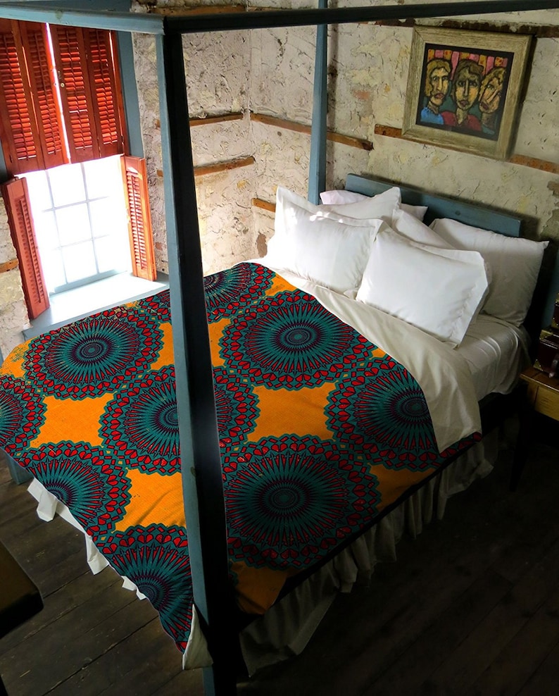 May include: A bed with a vibrant orange, teal, and red patterned comforter. The bed has a white bed skirt and is framed by a blue canopy. White pillows and a painting hang above the bed. The room has a rustic feel with a window and wooden shutters.